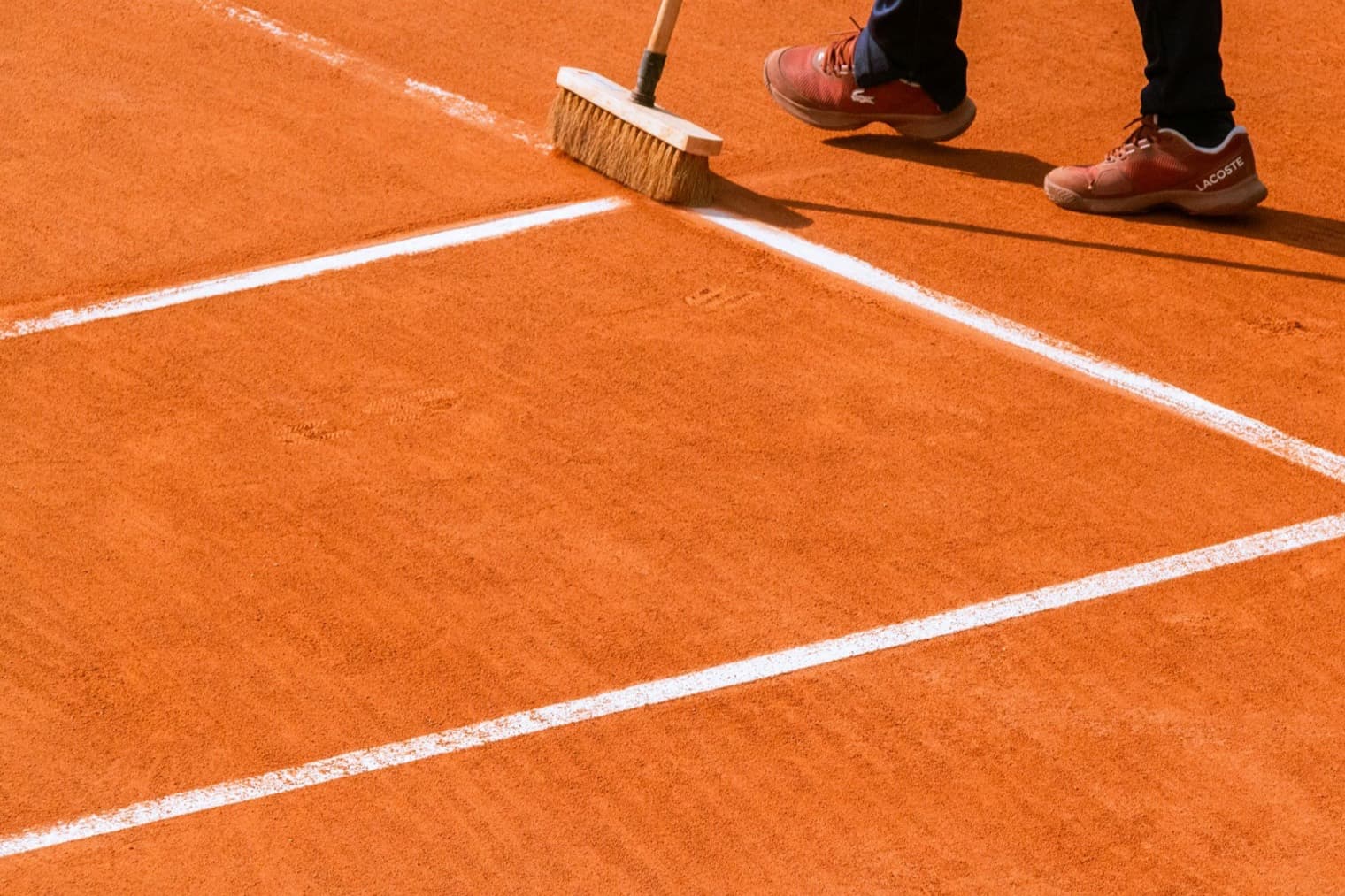 Groundskeeper sweeping the white lines on a freshly groomed clay tennis court