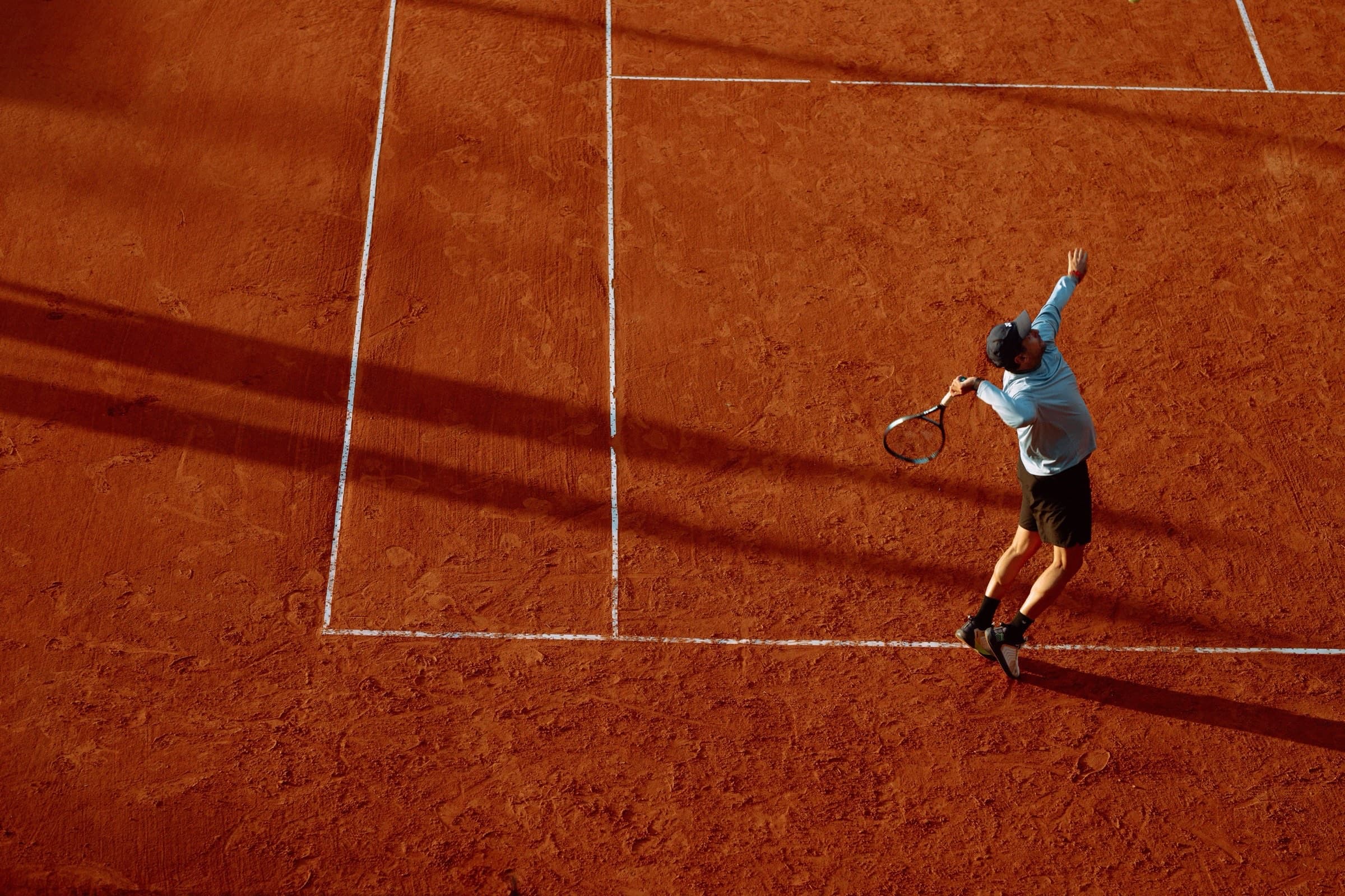 Clay tennis court at Meru Clay, a player serving in the low Arusha sun